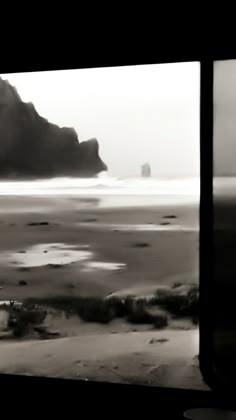 a black and white photo of the ocean with rocks in the distance from a train window