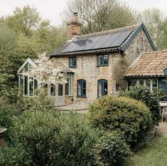 an old stone house with solar panels on the roof and windows, surrounded by greenery