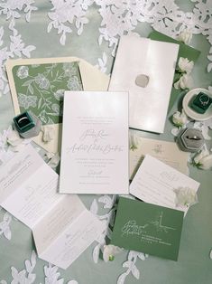 the wedding stationery is laid out on top of the bed with white flowers and greenery