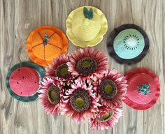 four crocheted sunflowers and three hats on a wooden surface