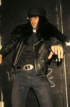 a man in black leather jacket and hat standing on stage with his hands out to the side