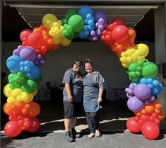 two people standing in front of an arch made out of balloons