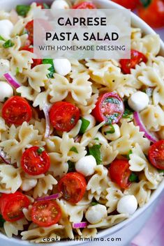 a white bowl filled with pasta salad next to cherry tomatoes and green onion wedges