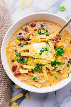 a white bowl filled with chili cheese and tortilla chips on top of a marble counter