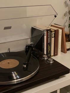 a record player sitting on top of a wooden table next to books and a plant