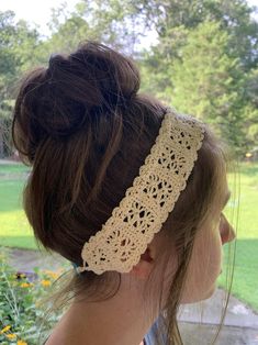 a woman wearing a crocheted headband in front of some flowers and trees