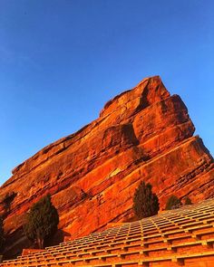 a large rock formation in the background with rows of seats on each side and trees at the base