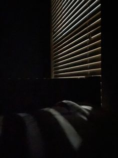 the light is shining through the blinds in the dark room with the bed and pillows