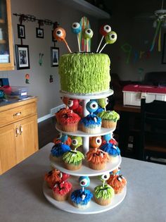 a three tiered cake decorated with cupcakes and monster eyes on it's sides