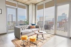 a living room filled with furniture and large windows overlooking the cityscape in the distance