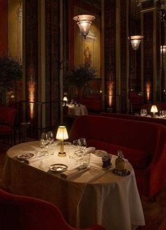 a dining room with red chairs and white table cloths, lit by lamps on either side