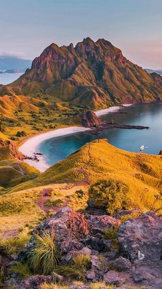 an aerial view of mountains, water and sand from the top of a grassy hill