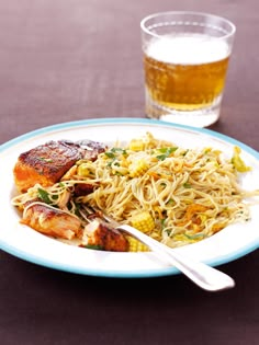 a white plate topped with meat and noodles next to a glass filled with beer on top of a table