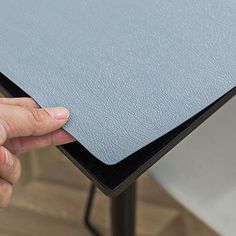 a hand is holding the edge of a table with a blue leather cover on it