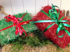 two red and green christmas balls with bows on top of hay bales in front of a white wall