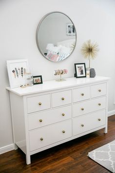 a white dresser topped with lots of drawers under a round mirror on top of it