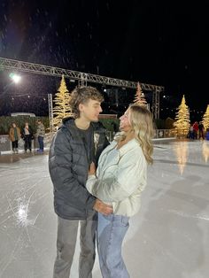 a man and woman standing on an ice rink at night with lights in the background