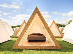 there is a bed in the middle of three pyramids on the grass with tents behind it