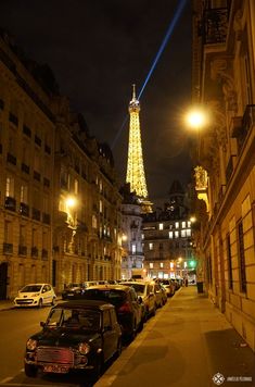 the eiffel tower is lit up at night in paris, with cars parked on the street