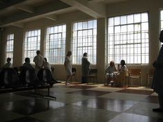 several people are standing in an empty room with chairs and checkered tile flooring