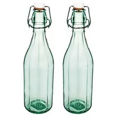 two green glass bottles sitting next to each other on a white background, one has a corked top and the other is empty