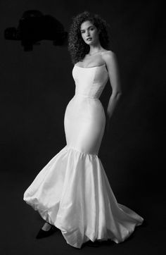 a woman in a long white dress posing for a black and white photo with her hands on her hips