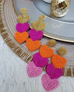 three heart shaped beaded earrings sitting on top of a table next to a gold plate