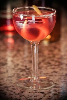 a close up of a drink in a wine glass on a table with bottles behind it