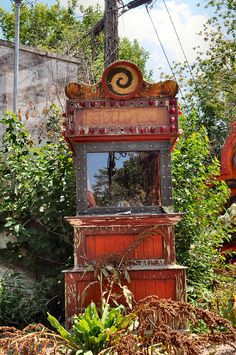 an old wooden clock tower sitting in the middle of some bushes and trees on a sunny day