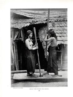 two women standing next to each other in front of a hut