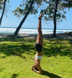 a woman is doing a handstand in the grass by the beach with trees