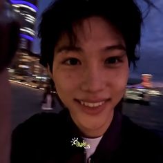 a young man smiling at the camera in front of a cityscape and water