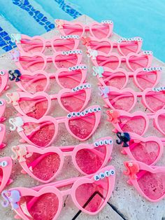 many pink sunglasses are lined up on the side of a swimming pool with name tags attached to them