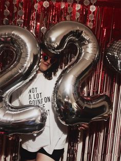 a woman holding two silver balloons in front of a red curtain with the number 20 printed on it