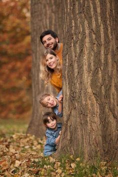 a family hugging each other in front of a tree with leaves on the ground around them