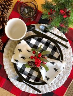 a christmas table setting with pine cones, holly berries and plaid napkins on a black and white plate