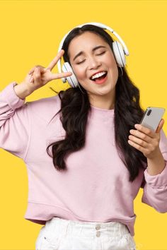 a woman wearing headphones and listening to music on her cell phone while standing in front of a yellow background