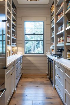 a kitchen with white cabinets and wooden flooring next to a large window that has open shelving on both sides