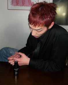 a young man with red hair sitting at a table and looking at his cell phone