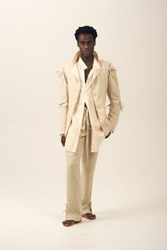 a man standing in front of a white background wearing a beige suit and tie with his hands in his pockets