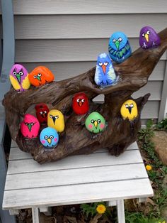 several colorful birds sitting on top of a piece of drifty wood next to a house