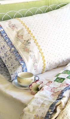 a cup and saucer sitting on top of a bed next to two pillow cases