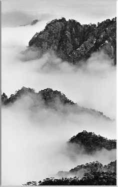 black and white photograph of mountains covered in fog with low lying clouds on the ground