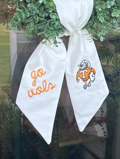 two white ties with orange letters on them hanging from a window sill in front of a potted plant