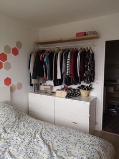 a bedroom with a bed, dresser and clothes on hangers above the headboard