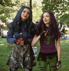 two women dressed up in costumes standing next to each other on the grass, one holding an apple