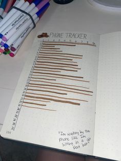 a notebook with some writing on it and several colored pencils next to the book