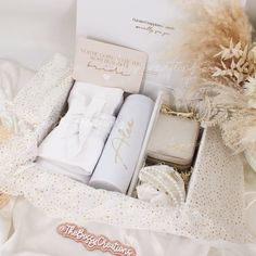 an open gift box filled with baby's clothes and blankets next to some flowers