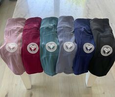 five different colored pants with silver emblems on them sitting on a white stand in front of a window