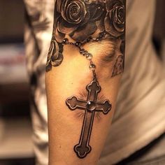 a man with a cross and roses tattoo on his arm is holding a rosary in front of him